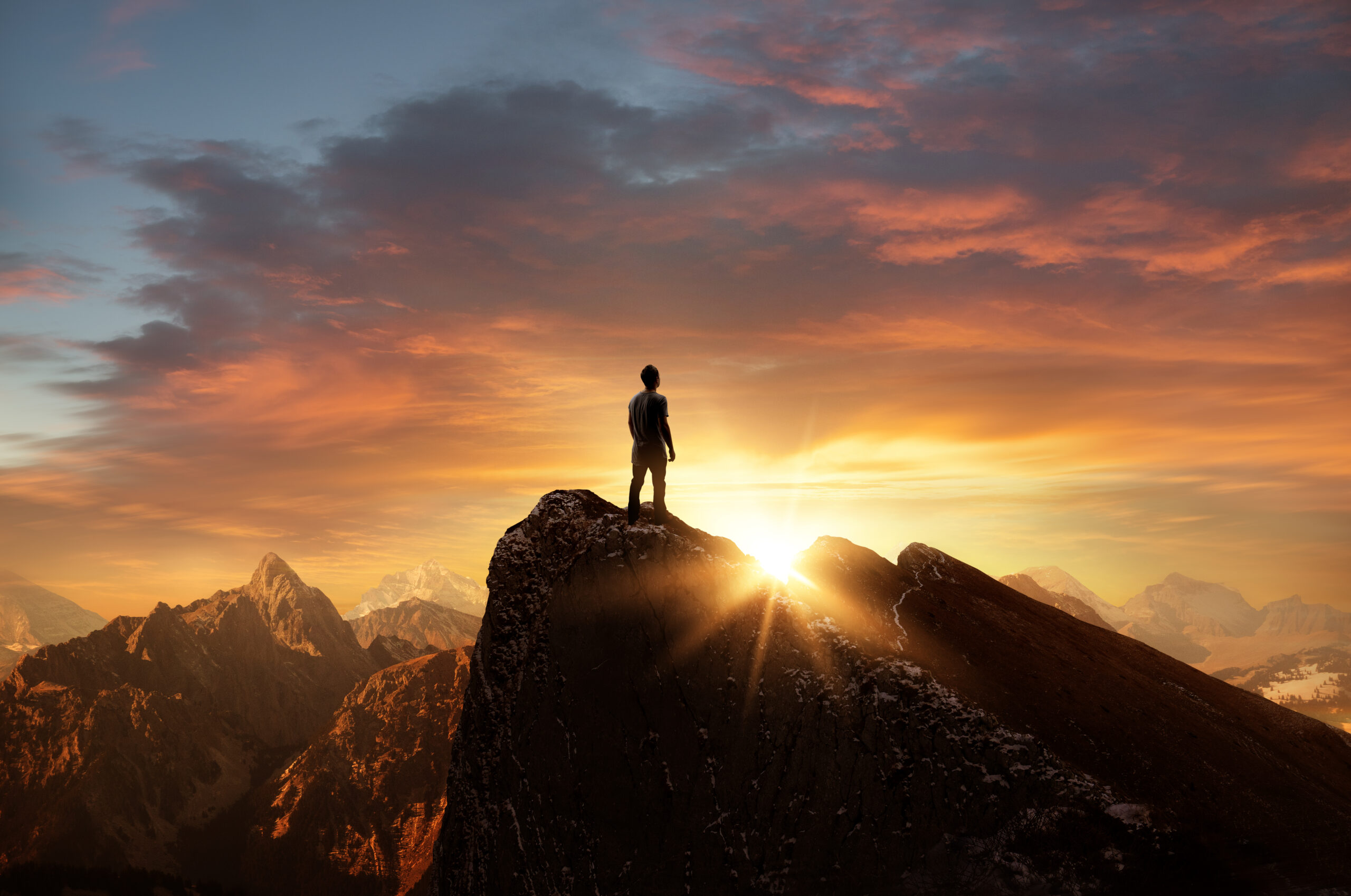 A person stands on a mountain peak during sunrise, surrounded by rugged mountains and dramatic clouds, golden sunlight streaming over the horizon—a moment capturing how to make change and start a quick guide for living a better life.