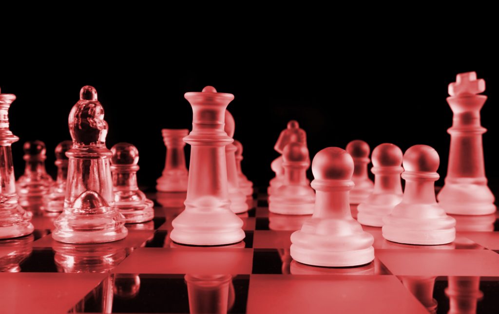 A glass chess set with translucent pieces is arranged on a chessboard. The image has a red tint and dark black background, symbolizing how Drifters in Outwitting the Devil must make bold moves to stop drifting and start living the life they want.