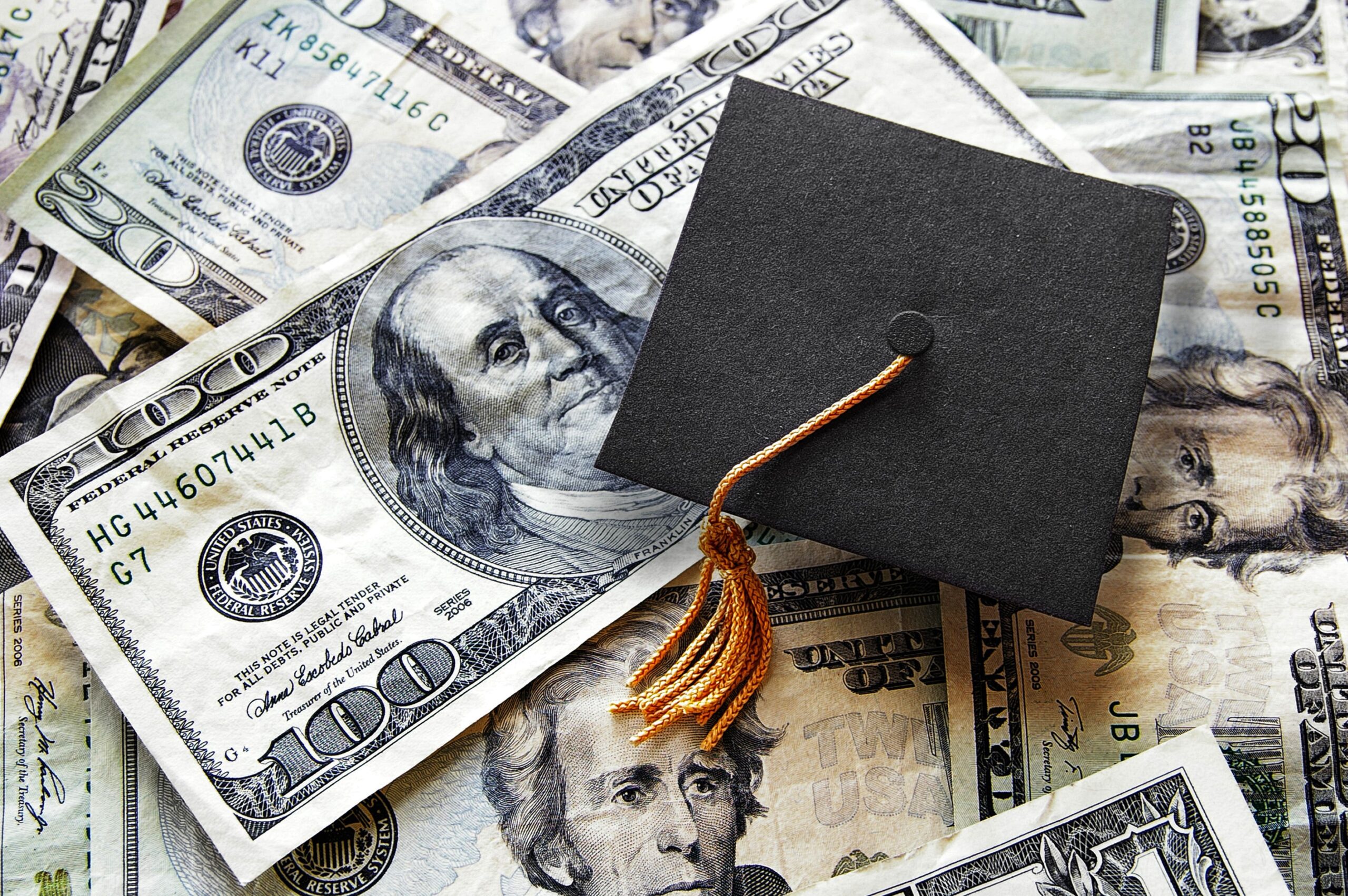 A graduation cap with a gold tassel rests on a pile of U.S. dollar bills, including $100 and $20 notes, symbolizing the cost of education—and the need to navigate student loan repayment with confidence.