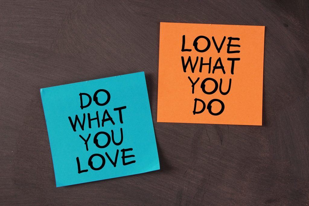Two sticky notes on a dark surface: one blue note reads DO WHAT YOU LOVE, and one orange note reads LOVE WHAT YOU DO—perfect reminders for balancing passion and practicality every day.