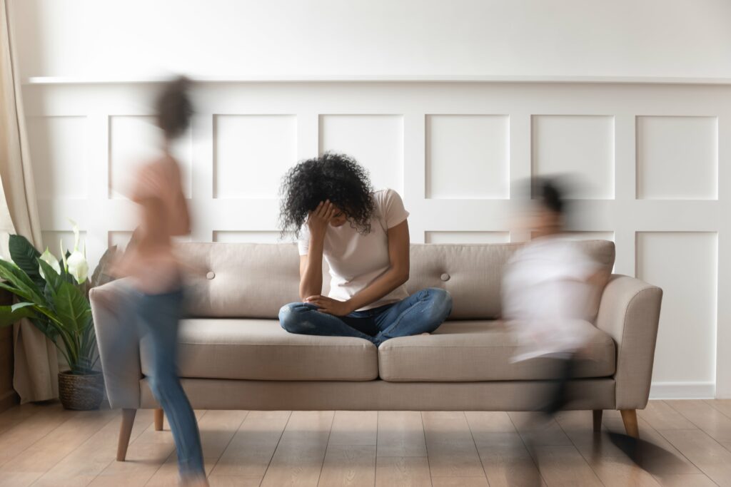 Woman sitting on couch with blurry kids running by her.