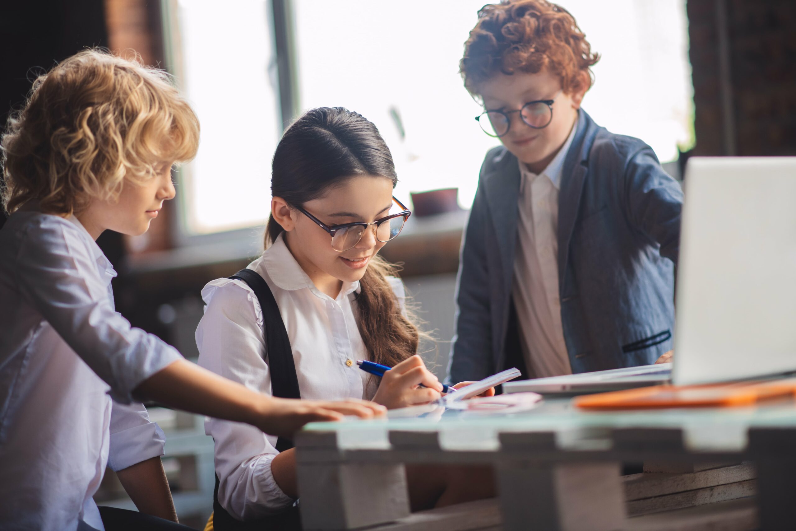 Three children dressed professionally looking at a workbook