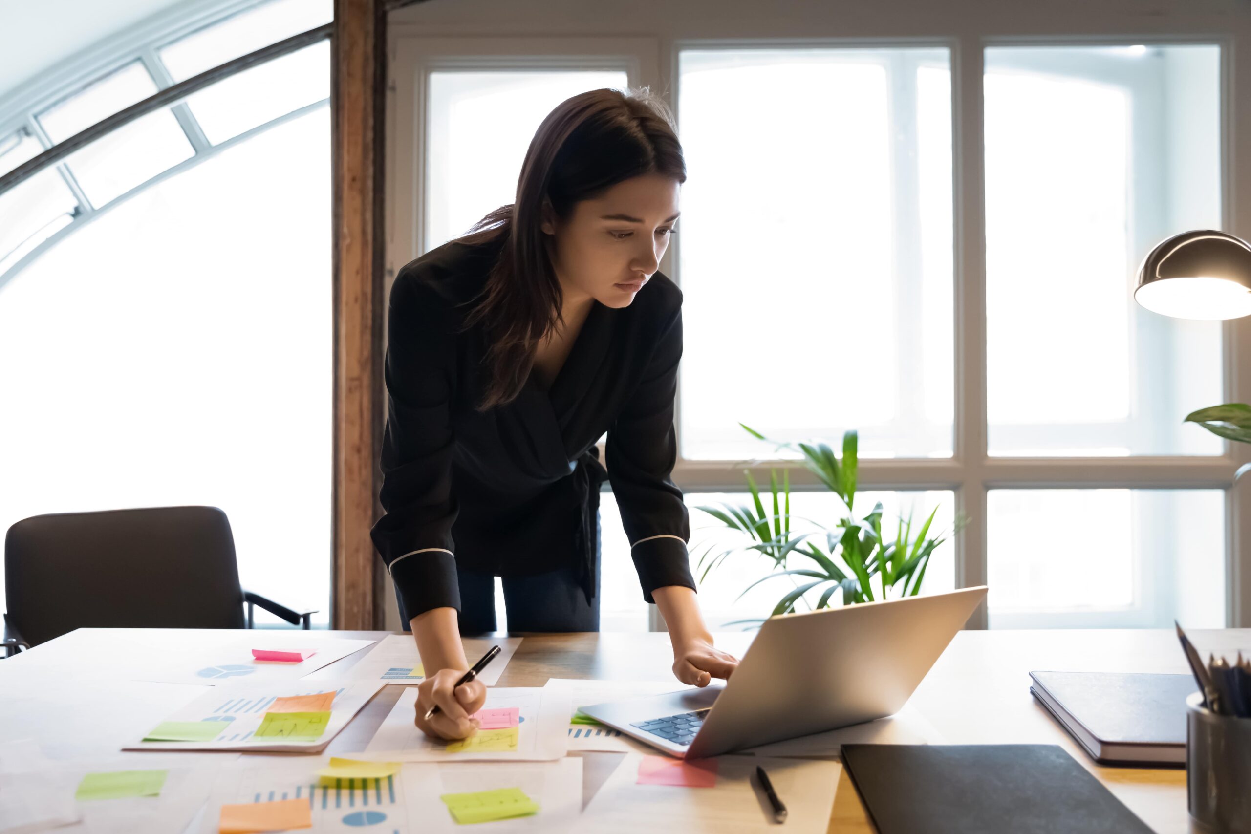Woman stands over work desk in black suit