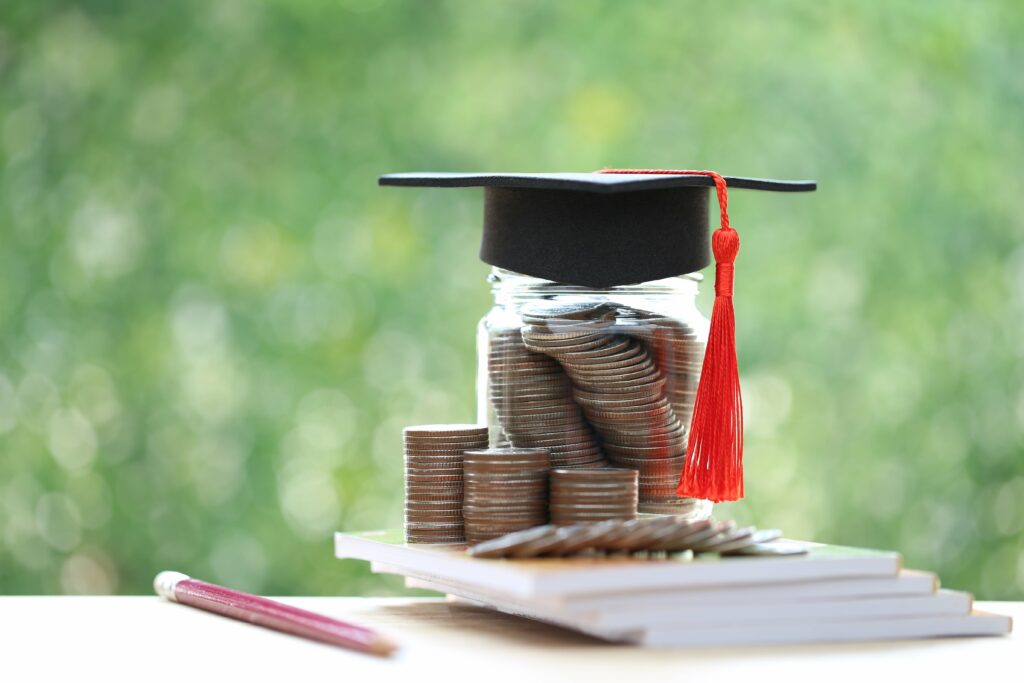 Graduation hat on coins money in the glass bottle on natural green background