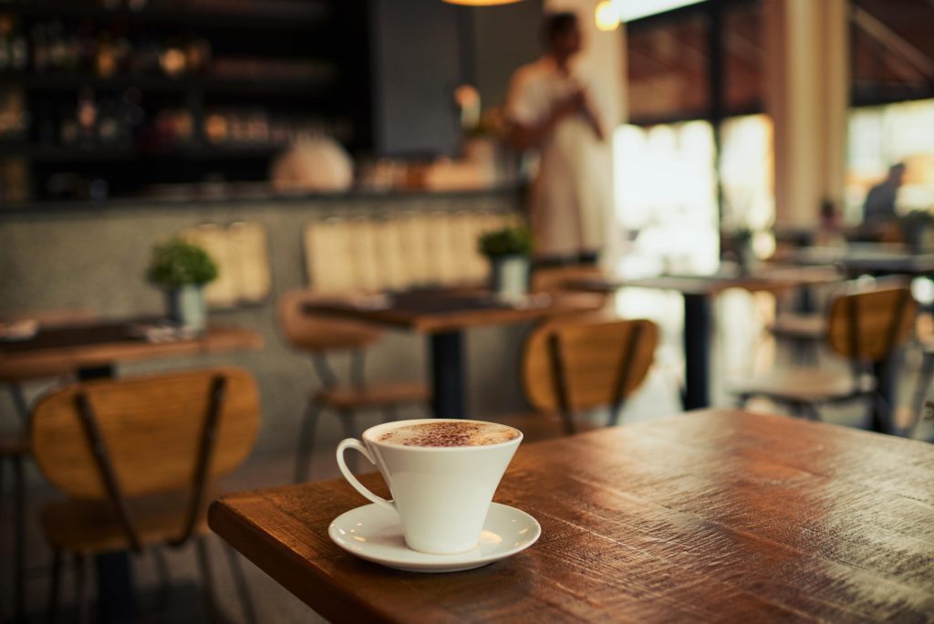 white coffee cup on the edge of a wooden table in a cafe.