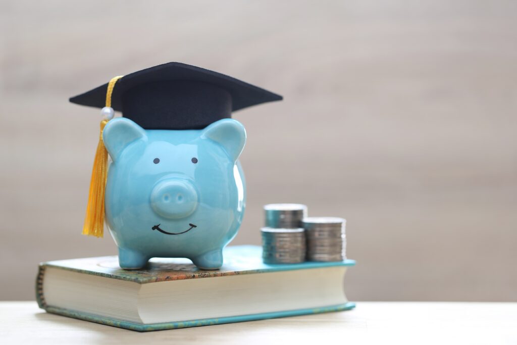 Blue piggy bank on top of textbook wearing a graduation cap.