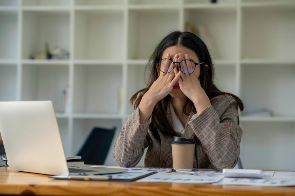 woman with hands covering eyes sitting at messy office desk