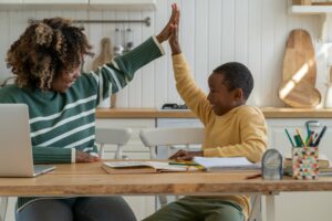 A woman high-fiving a young boy when helping with his homework.