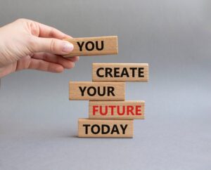 "You create your future today" printed in red and black text on wooden blocks. 