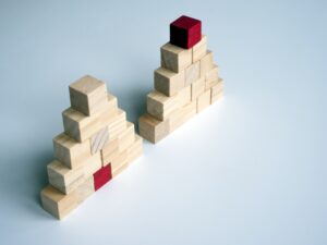 Wooden blocks stacked in two pyramid shapes with a red block placed at in the bottom row for one and the red block placed on the top for the other.