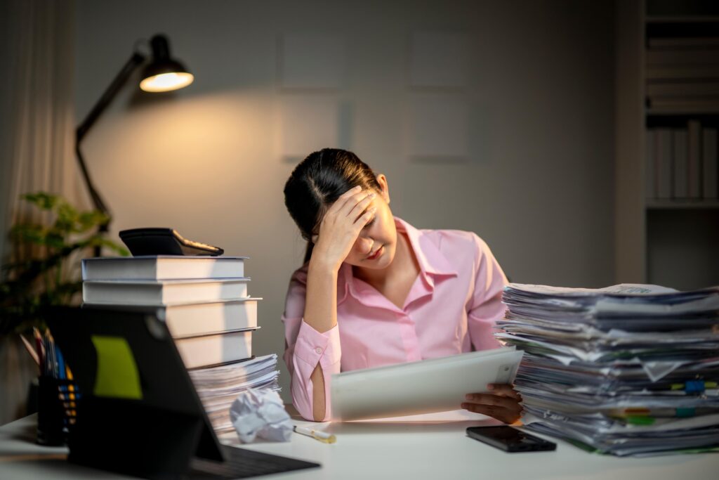 A woman sitting at her desk with her hand on her head looking at a document.