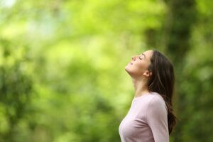 A woman in nature looking up to the sky with her eyes closed. 