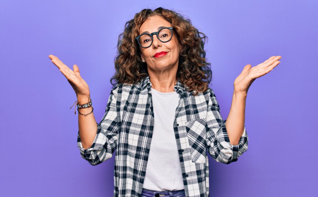 woman stands in front of purple background and shrugs her shoulders