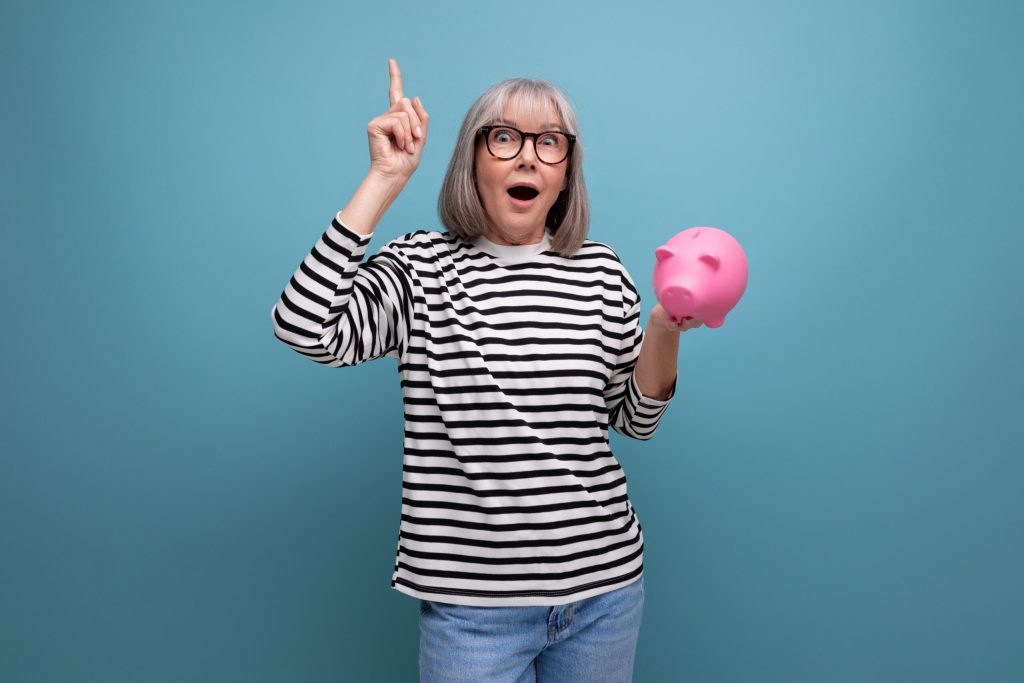An excited woman with her one hand up and the other holding a pink piggy bank