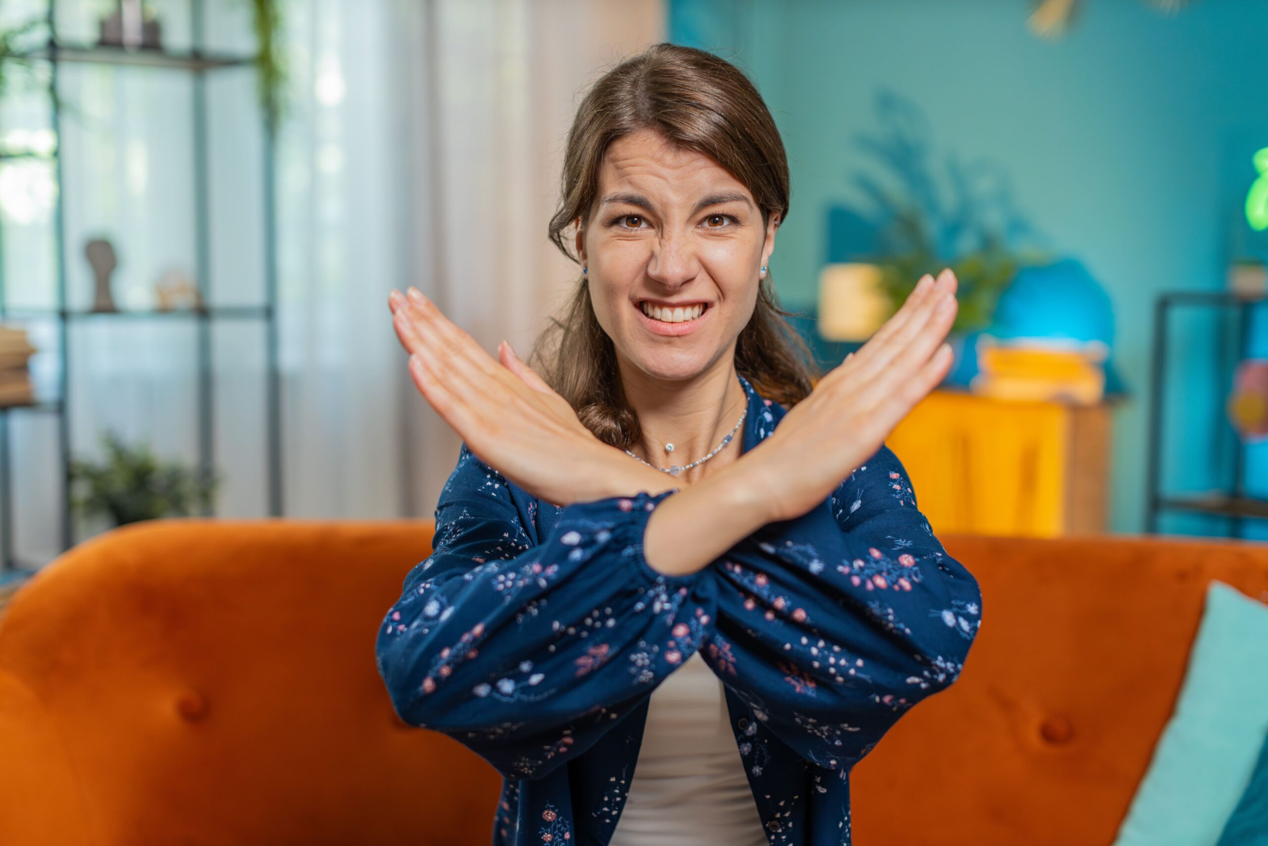 Woman sitting on a sofa with a frustrated expression, crossing her arms in an “X” gesture to indicate refusal or disapproval.