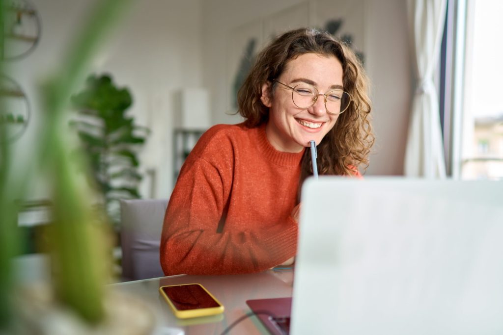 Young woman enjoying a calm, productive lifestyle while working from home, smiling during a video call in her cozy workspace.