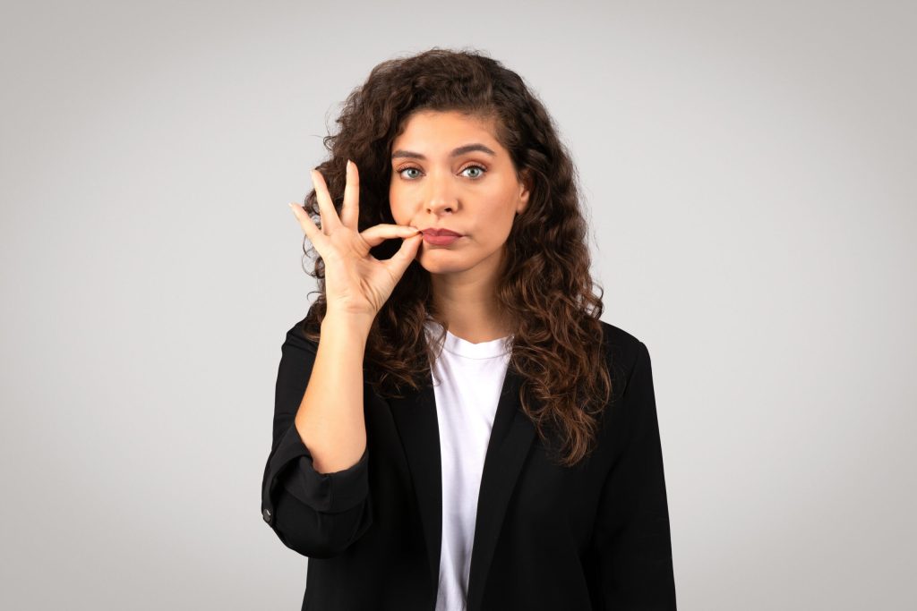 Confident woman making a zip-it gesture, illustrating how strategic silence and restraint can be powerful tools for success.