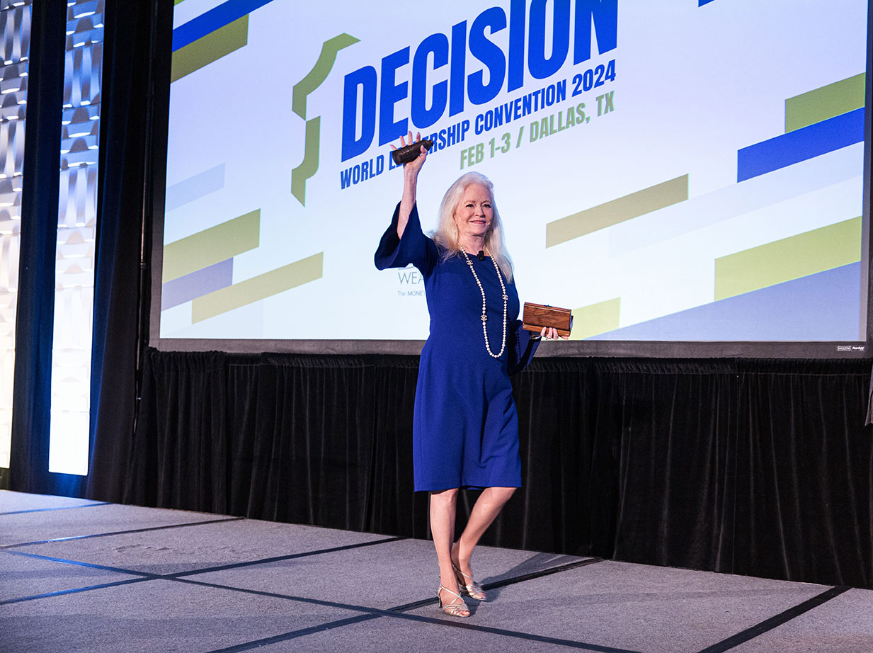Sharon Lechter in a blue dress speaking at a Decision World Leadership Convention