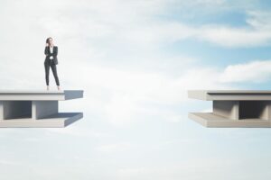A woman in a business suit stands thoughtfully on the edge of a floating platform, facing a gap to another similar platform, against a bright sky.