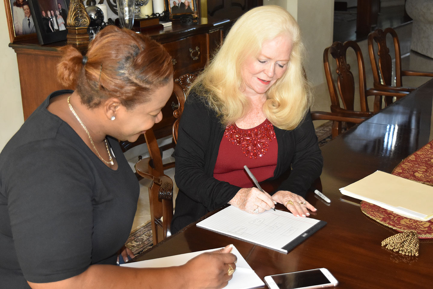 Sharon sitting writing down notes on a notepad with a woman for one on one mentoring
