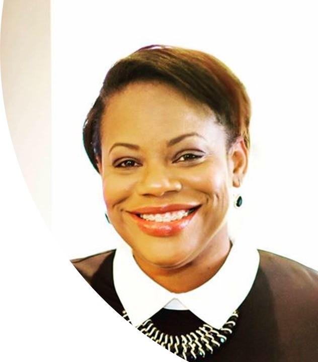 A woman with short dark hair, wearing a black top with a white collar and a silver necklace, smiles at the camera against a bright, white background.