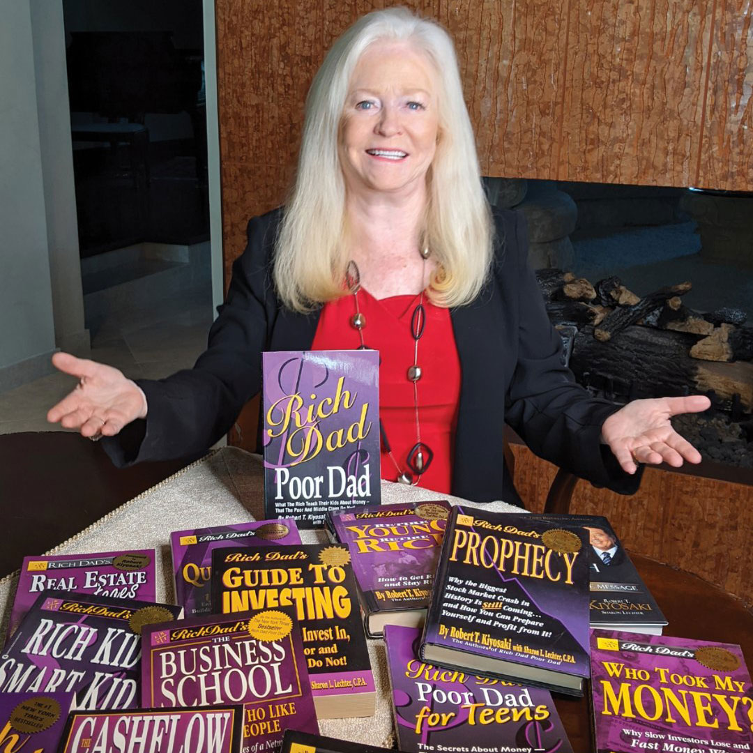 Sharon Lechter showcasing a collection of financial books on a table, including Rich Dad Poor Dad