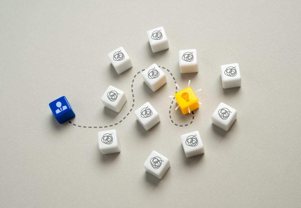A blue cube with a person icon is connected by a dashed line to a yellow cube with a lightbulb icon, surrounded by white cubes with swirling patterns.